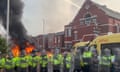 A fire burns behind a line of police officers in riot gear