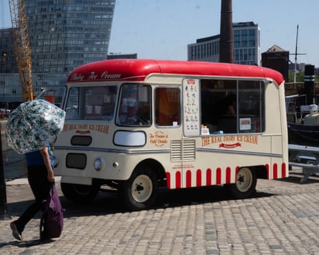 A woman, next to an ice cream truck, shelters from the sun with an umbrella in Liverpool, United Kingdom.