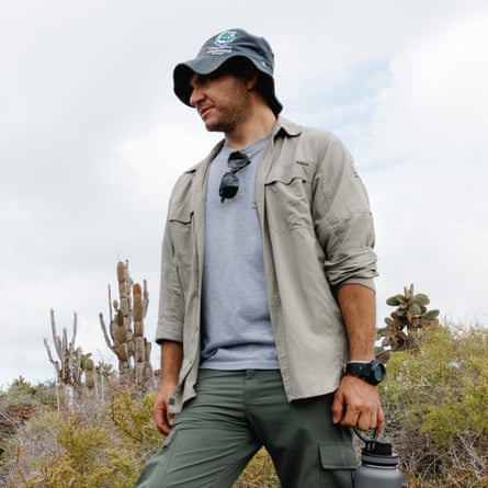 A young Hispanic man stands on a hillside with cactii and scrubby vegetation behind him