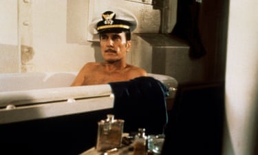 Duvall sitting in a bath wearing a white navy hat