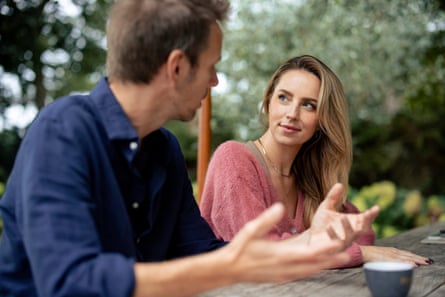 A man talking to a woman sitting at table in a garden