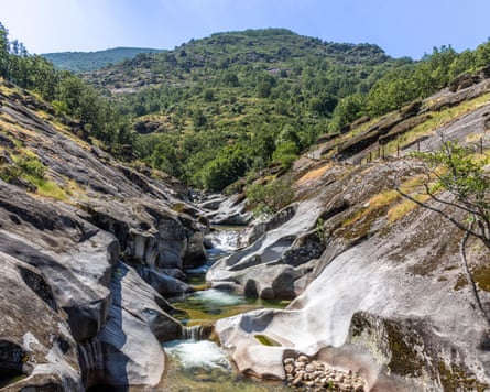A rocky river with little pools formed by granite boulders and wooded hills in the distance
