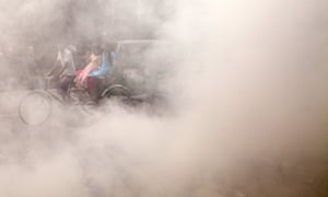 A Bangladeshi rickshaw puller rides past smoke created by burning waste materials on a street in Dhaka.