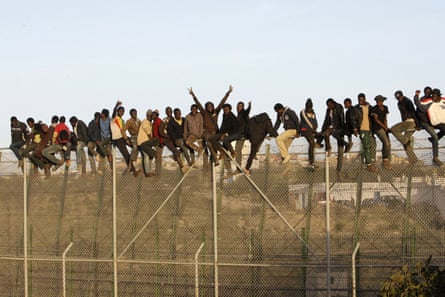 Migrants sit on top of a fence as they attempt to reach Melilla, the Spanish enclave on the north African coast, in October 2014.