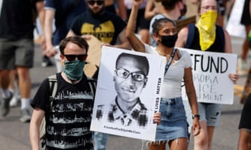 Man in sunglasses and mask holds image of Elijah McClain during rally