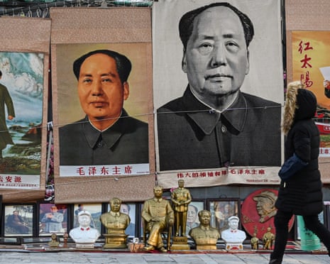 A woman walking past an antiques stall selling large posters of Mao Zedong.