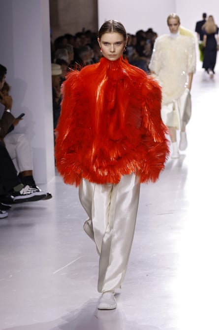 A model wearing a voluminous textured red coat with white satin trousers.