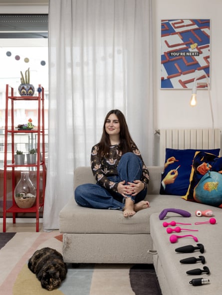 Portrait of Enrica sat on a sofa with her sex toys laid out in front of her