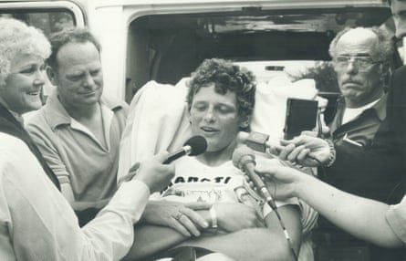 a man speaks into microphones while laying on a gurney outside an ambulance
