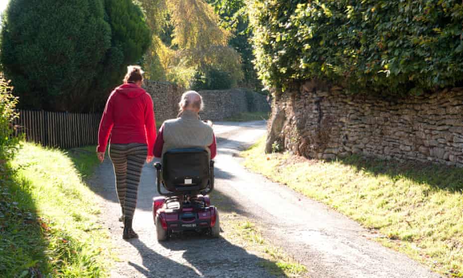 Man using a mobility scooter with his carer walking beside