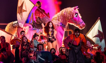 A pop star with red hair performs in front of a giant pink pony