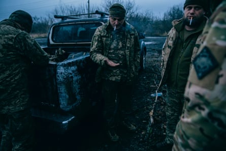Soldiers stand next to a truck and smoke cigarettes