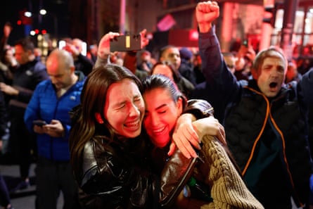 Two young women embrace with joy in a crowd at night