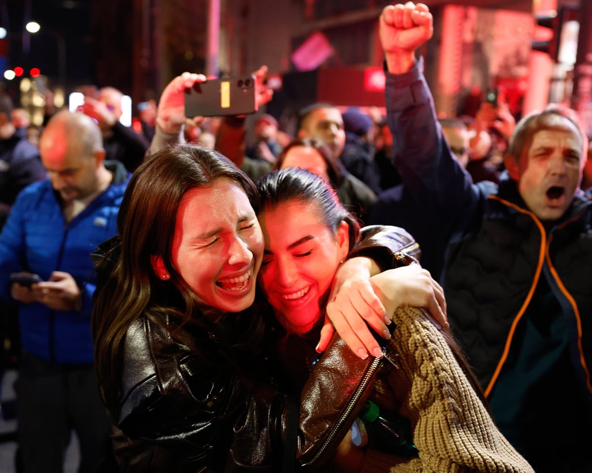 Two young women embrace with joy in a crowd at night