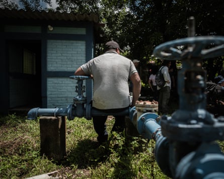 A man sits on a blue pipe with his back to the camera.