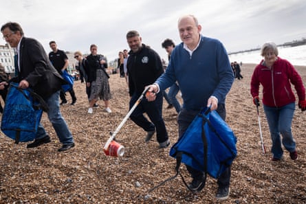 Ed Davey carrying a rubbish bag and using a litter-picker to collect a drinks can on Brighton beach