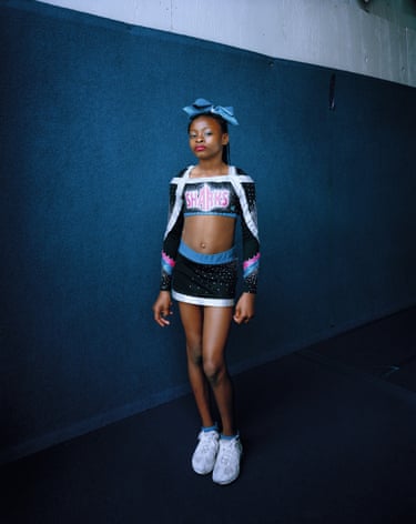 Young woman in cheerleading costume with a bow in her hair looks cautiously into the camera