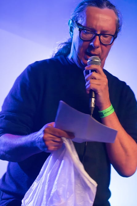 Steve Hill holding a microphone, paper, and plastic bag