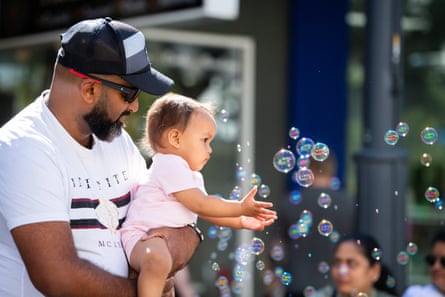 A man holds his baby daughter as she reaches out to bubbles floating in the air
