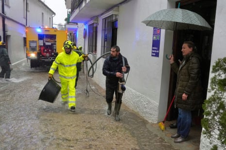 A firefighter assists citizens on a flooded street with ankle-deep water