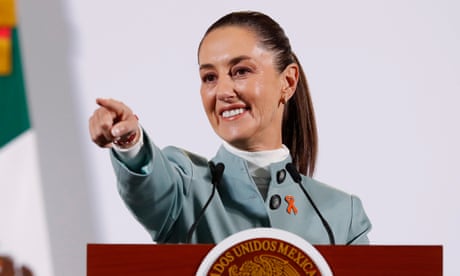A woman wearing a light blue jacket smiles and points at a lectern