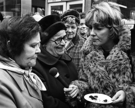 Esther Rantzen with a microphone outdoors interviewing two women