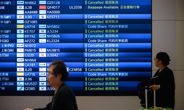 Travellers walk past an arrival board showing cancelled flights at Haneda airport in Tokyo.