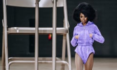 A model walks past a giant table and chairs wearing a purple zipped hoodie and matching hot pants