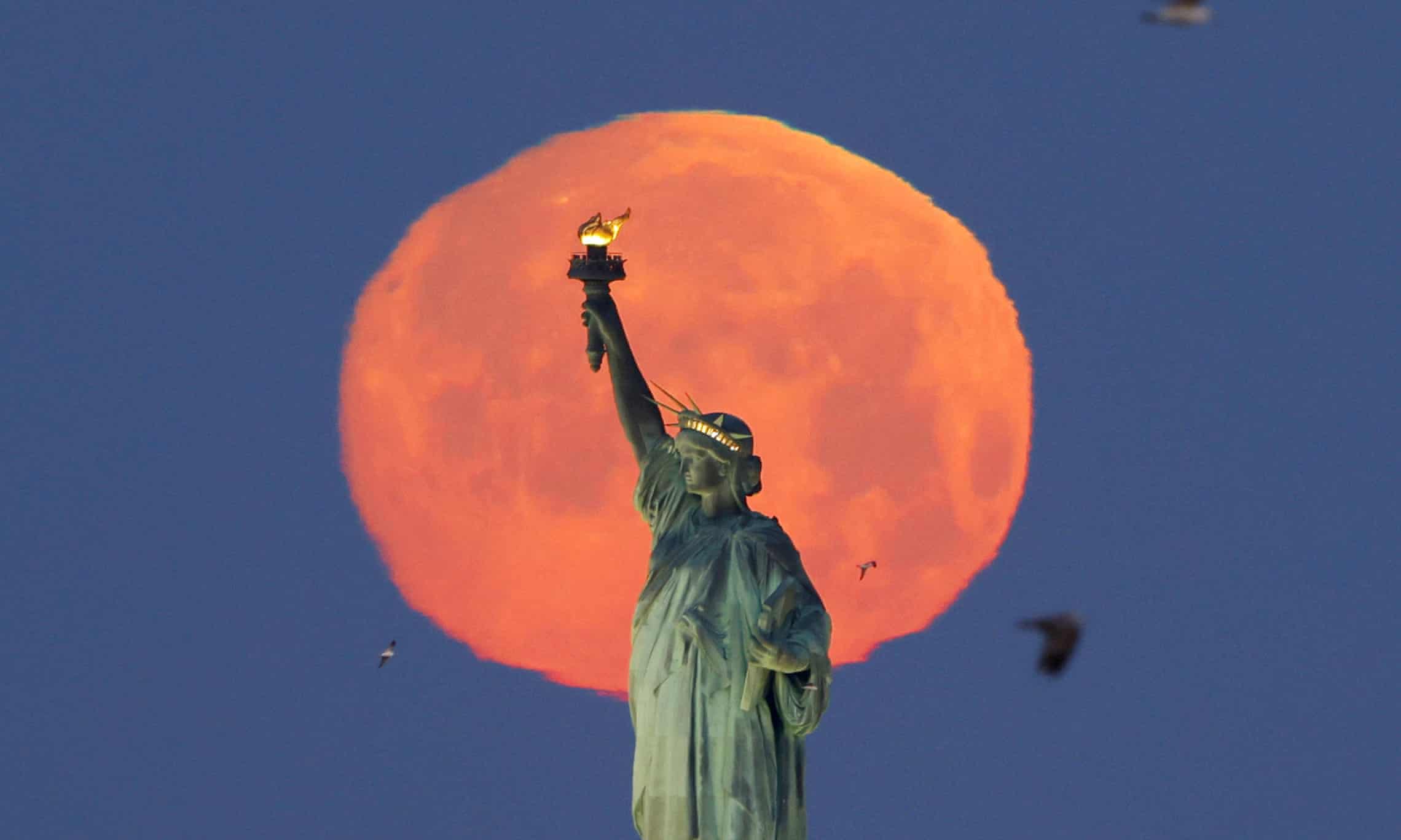 A pink supermoon sets behind the Statue of Liberty in New York City, New York A pink supermoon sets behind the Statue of Liberty in New York City, New York
