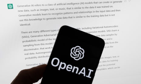 The OpenAI logo is seen on a mobile phone in front of a computer screen displaying output from ChatGPT