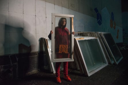 A woman in red holds a damaged window frame before her to create a framed portrait