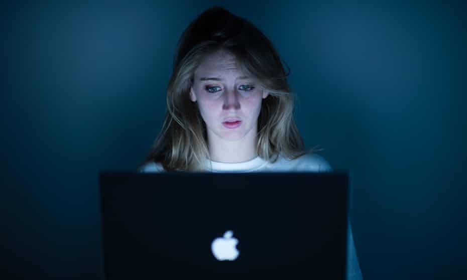 A young woman using a Apple laptop computer - looking scared worried harassed bullied anxious concerned<br>D9KRG8 A young woman using a Apple laptop computer - looking scared worried harassed bullied anxious concerned
