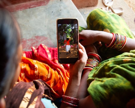 Two seated women are seen from above, one of whom is holding a phone showing an image of people on a swing