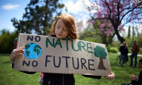 A girl looking down at a cardboard sign that says 'No nature, no future'