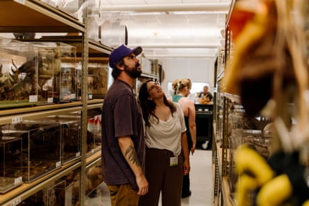A man and a woman stand between high shelves, looking up at something on a top shelf.