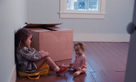 Little brown haired girl sitting on a suitcase in an empty room with one box and staring at her doll<br>A05HB3 Little brown haired girl sitting on a suitcase in an empty room with one box and staring at her doll