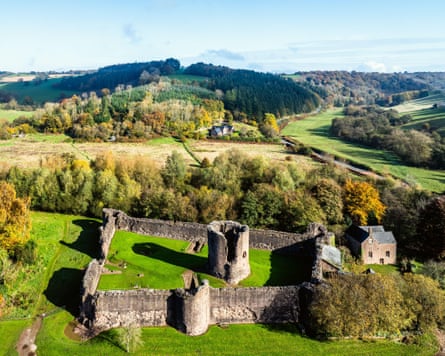 A small ruined castle, seen from above, with wooded hillsides beyond