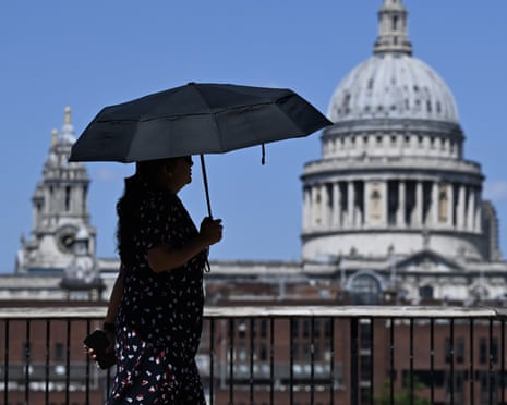 A woman shades herself with an umbrellas as she walks near St Paul's Cathedral