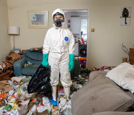 A woman dressed in a white protective suit wearing a mask and green gloves. Standing in a room full of debris