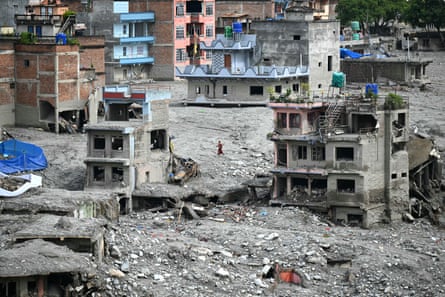A woman walks past damaged houses in the aftermath of the flash floods in Trishuli.
