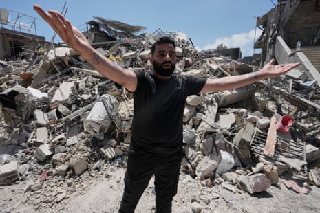 A man with his arms outstretched in protest near a destroyed building.