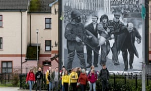 Tourists on a walking tour pass a mural depicting Bloody Sunday.