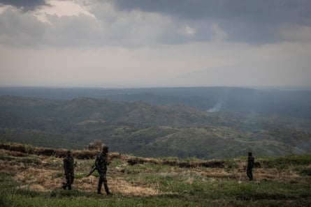 Three soldiers are seen on a ridge looking over forested hills