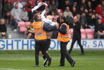 One of two anti-Gary Neville protesters is escorted off at Salford’s Peninsula Stadium