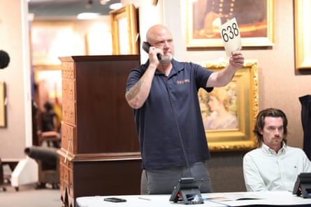 A person holds the number 638 while waiting tersely on the phone in an auction house