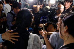 Members of the media gather around a person being interviewed, withe cameras and microphones. Someone has there arm around the person being interviewed