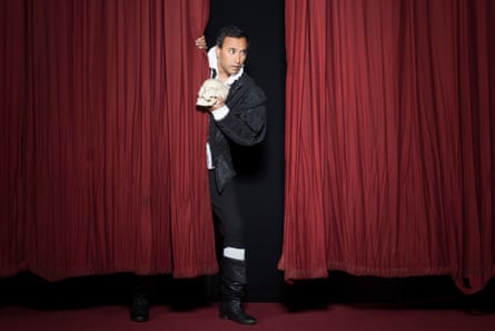 Rhik Samadder holding a skull and looking out from behind red stage curtains