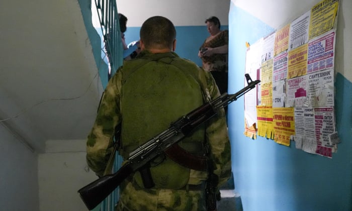 Residents cast their votes near a military member in the ‘referendum’ in Donetsk