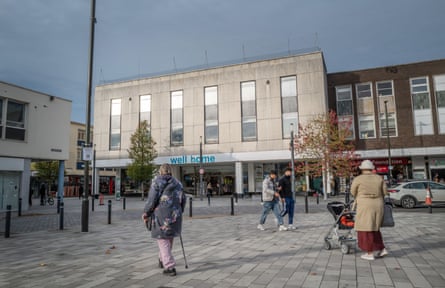 A woman pushing a pram and another supported by a walking stick cross a shopping precinct