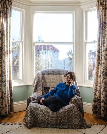 Emma Beddington sits in an arm chair on the phone, in front of a big bay window with sun shining.
